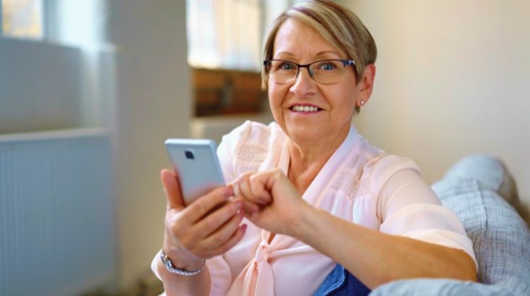 Feature | Portrait of cheerful senior woman using smartphone while sitting on sofa | Apps Your Parents Didn't Know They Needed