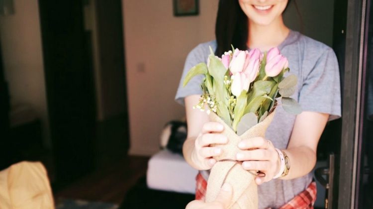 A smiling woman receiving flowers by the door | 7 Products Every Woman In Your Life Will Thank You For | Featured